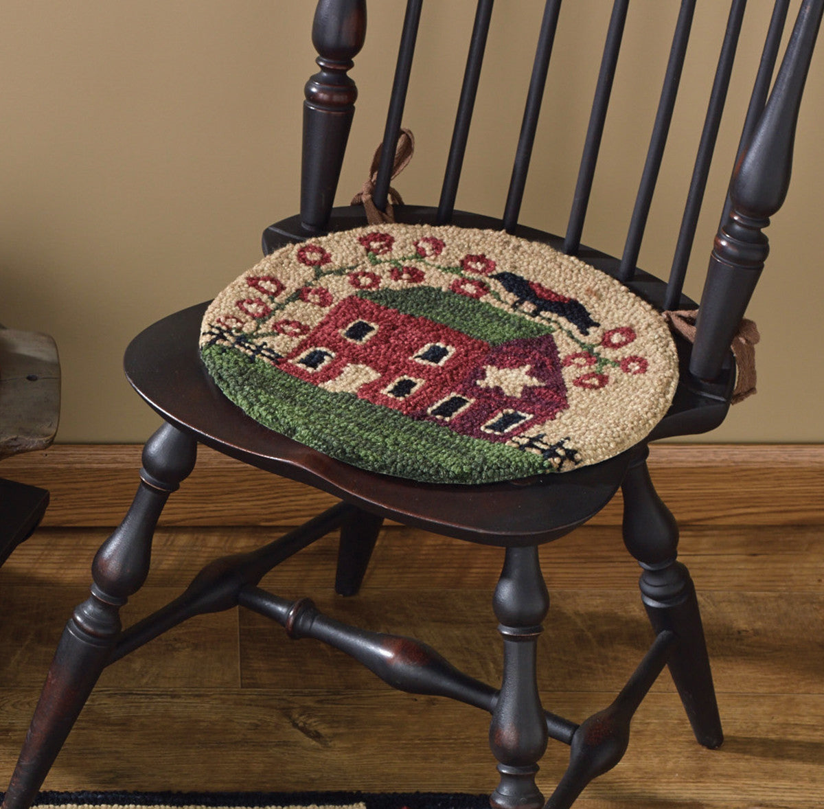 A hooked chair pad with a red house design, placed on a wooden chair.