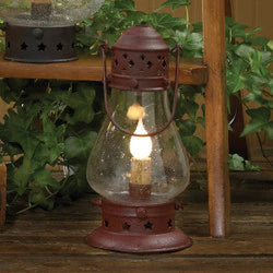 Vintage-style lantern with a lit candle on a wooden surface with greenery in the background