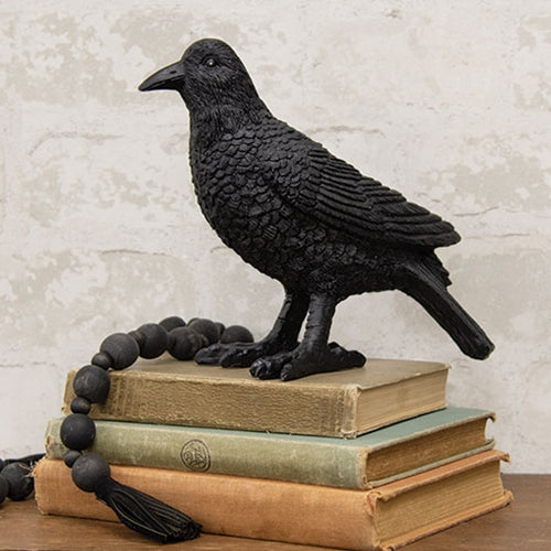 Black crow figurine on a stack of books with a textured wall background