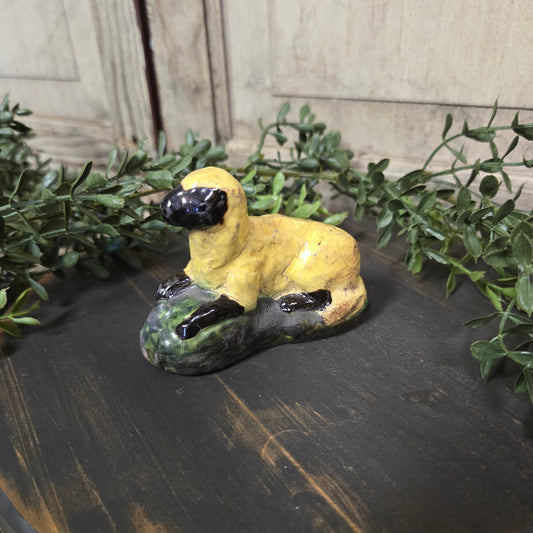 Pottery sculpture of a white sheep laying down on a wood surface with greenery