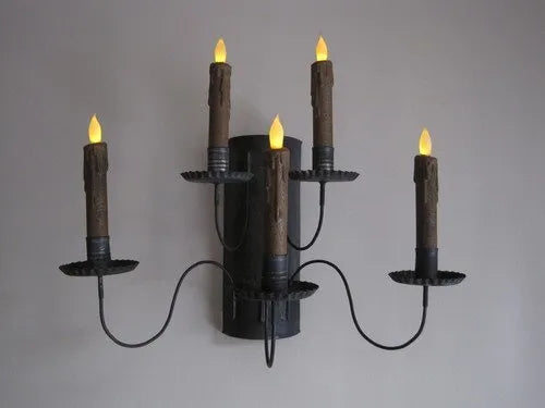 Black metal wall sconce with four candle-like lights on a gray background