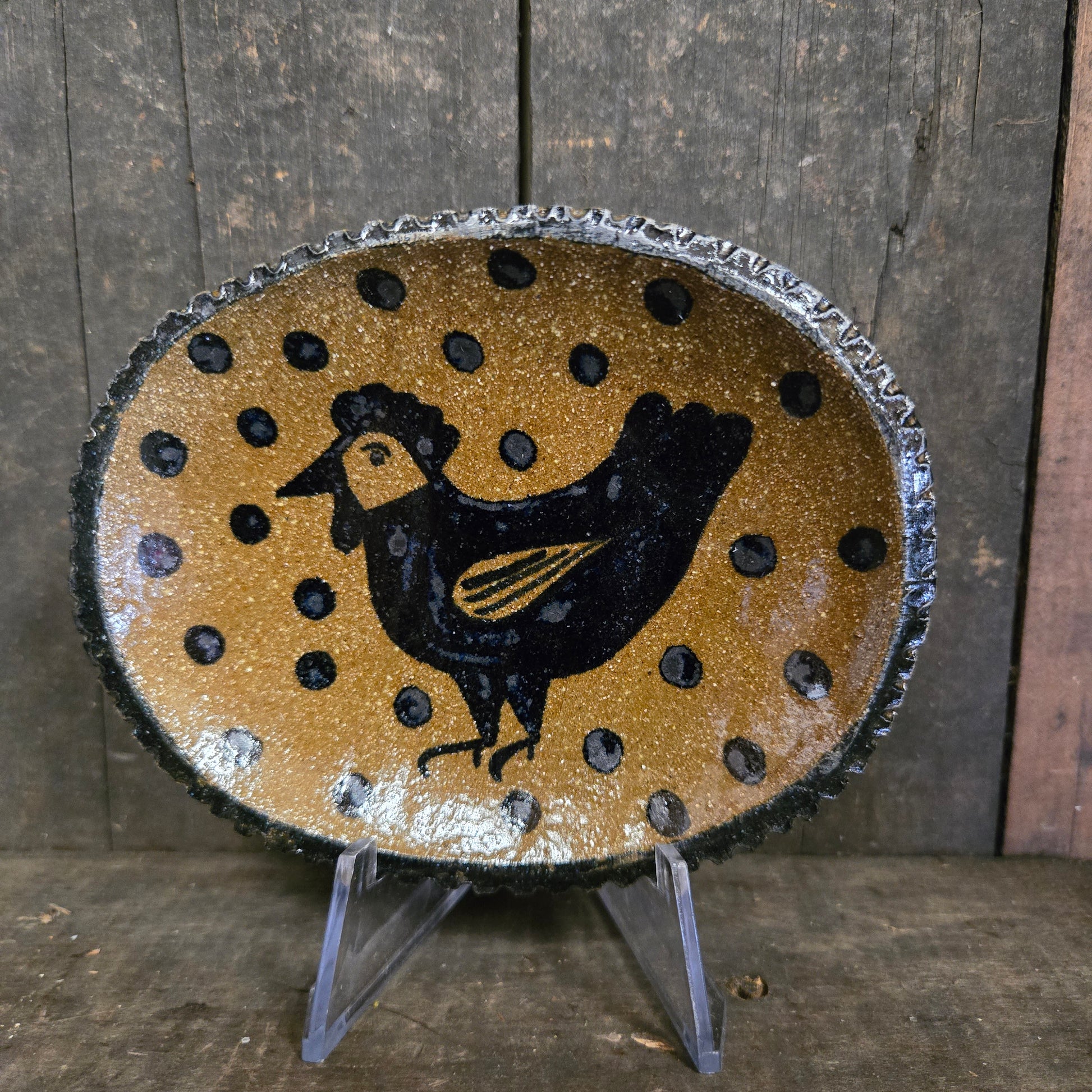 Decorative plate with a black animal silhouette on a gold background with black dots, placed on a wooden surface.