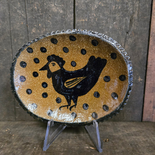 Decorative plate with a black animal silhouette on a gold background with black dots, placed on a wooden surface.