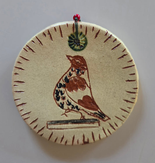 A handcrafted redware ornament featuring a bird design with a green string and red bead detail.