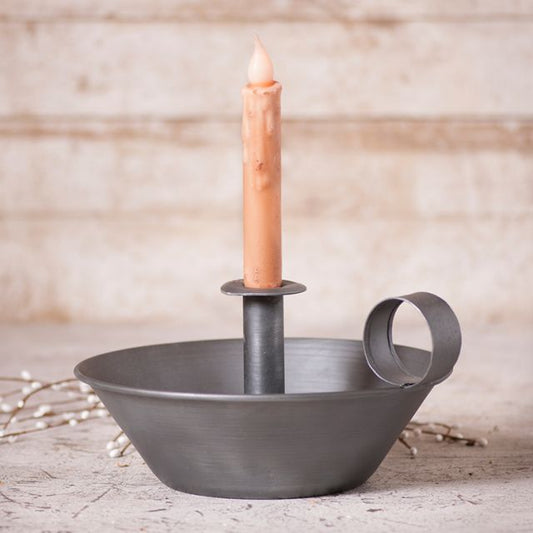 A Round Tapered Pan Candle Holder made of antique tin with a candle placed in the holder, displayed on a wooden surface with a decorative bow around it.