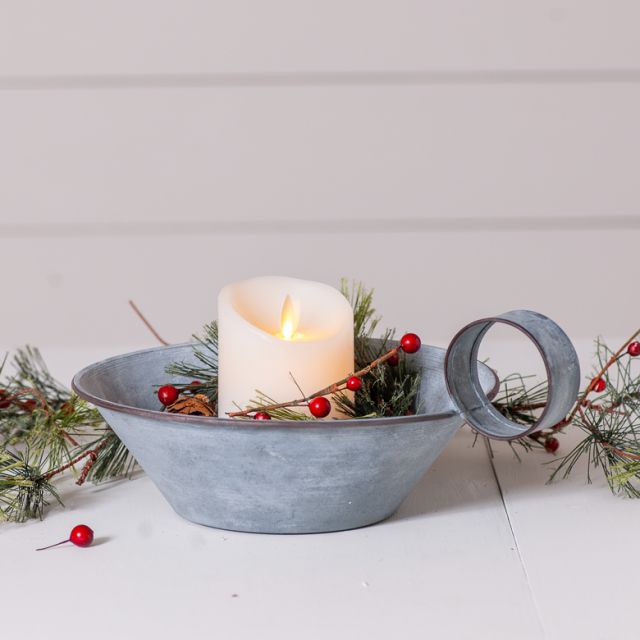 Decorative candle holder with a lit candle, greenery, and red berries on a light background