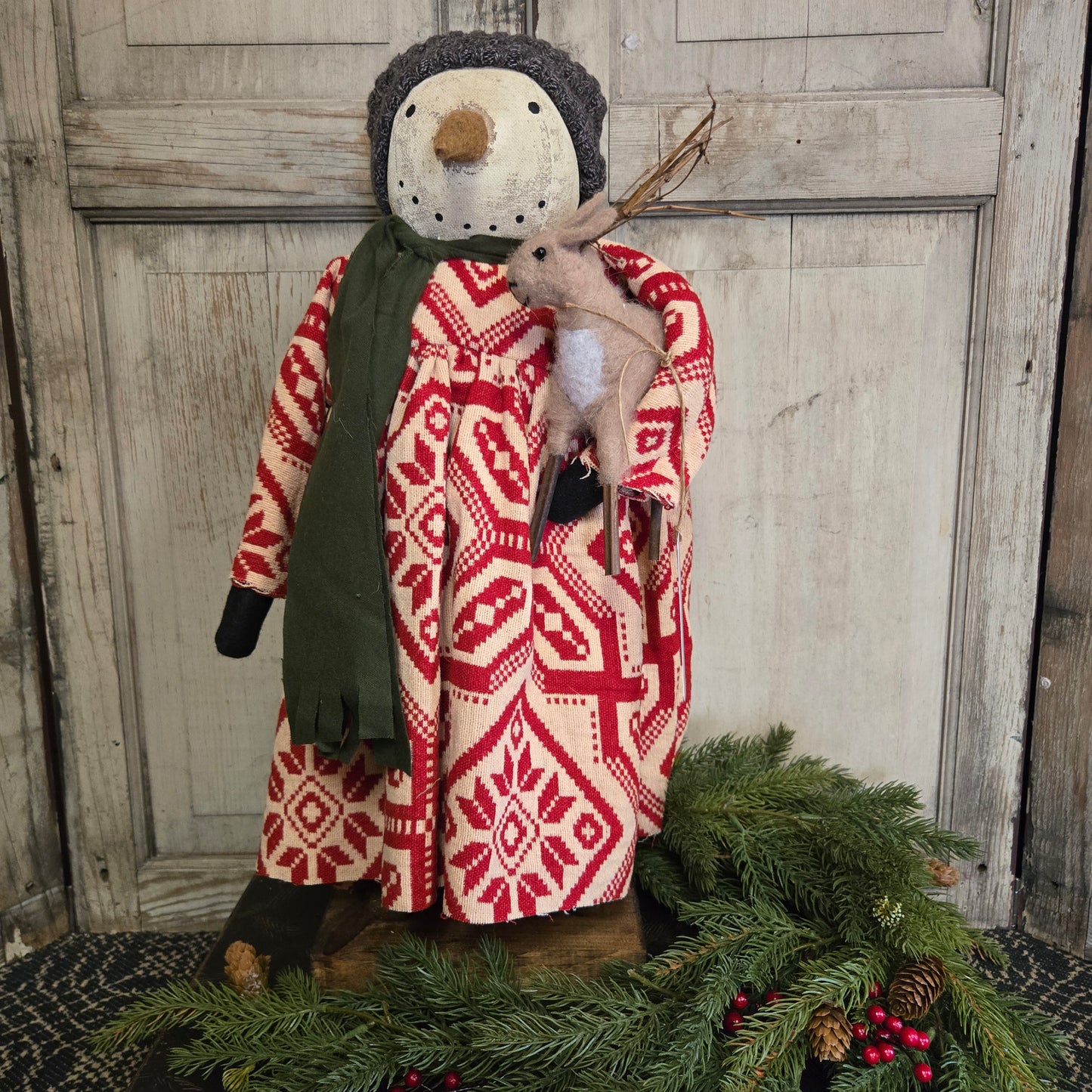 Decorative deer figure wrapped in a red and white patterned blanket against a wooden background.