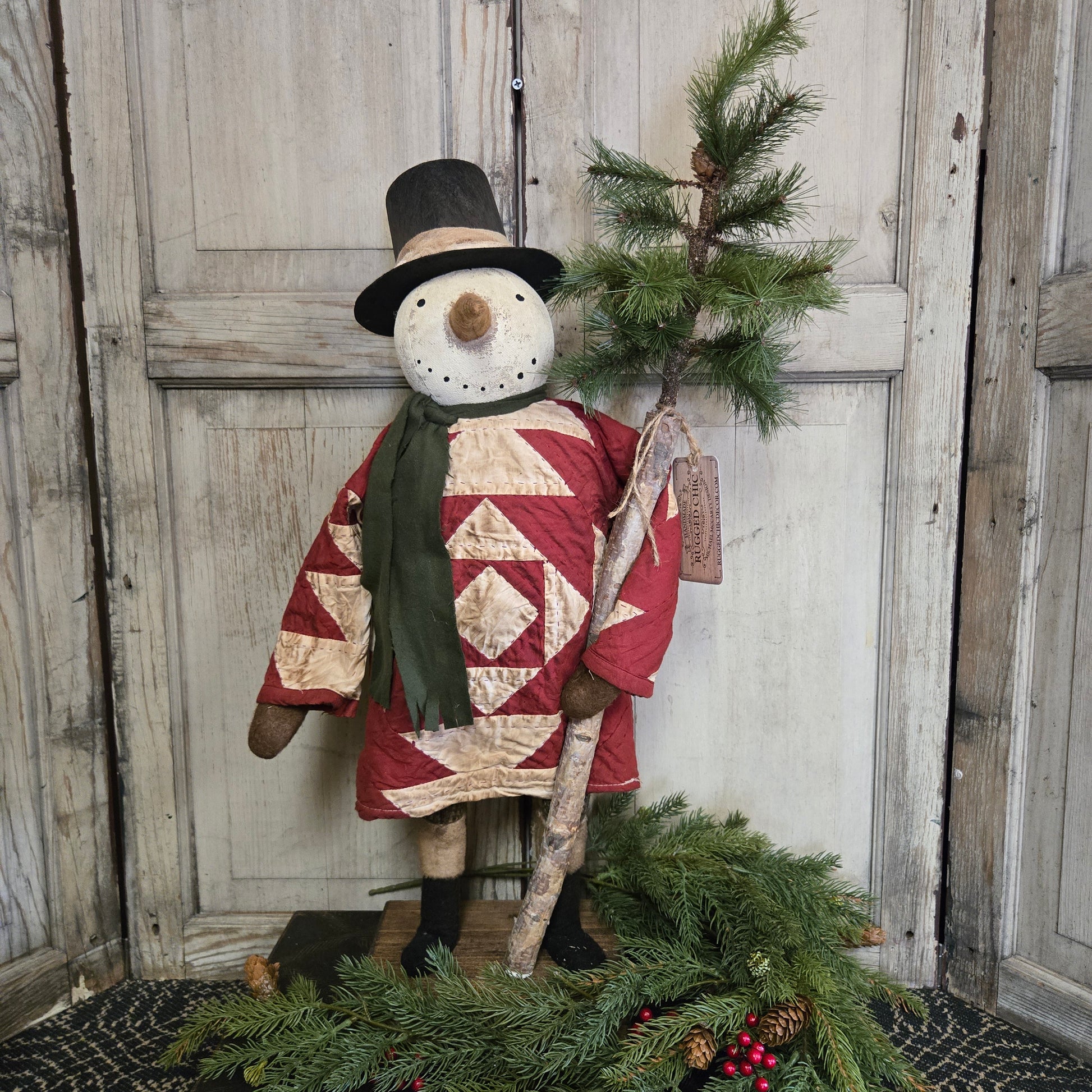 Decorative snowman with quilted design and pine branches on a wooden surface