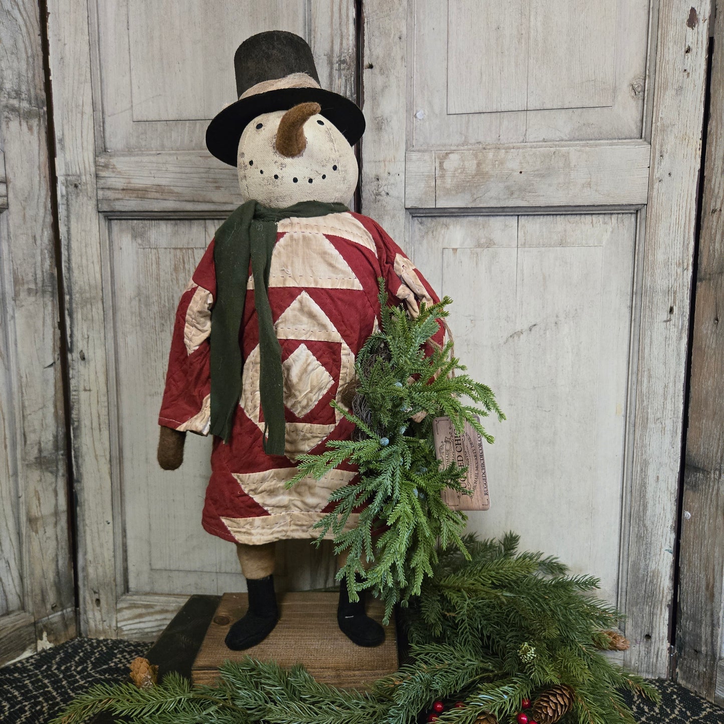 Decorative snowman figure with a quilted design and greenery against a wooden background