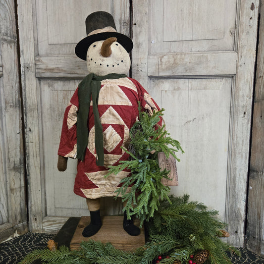 Decorative snowman figure with a quilted design and greenery against a wooden background