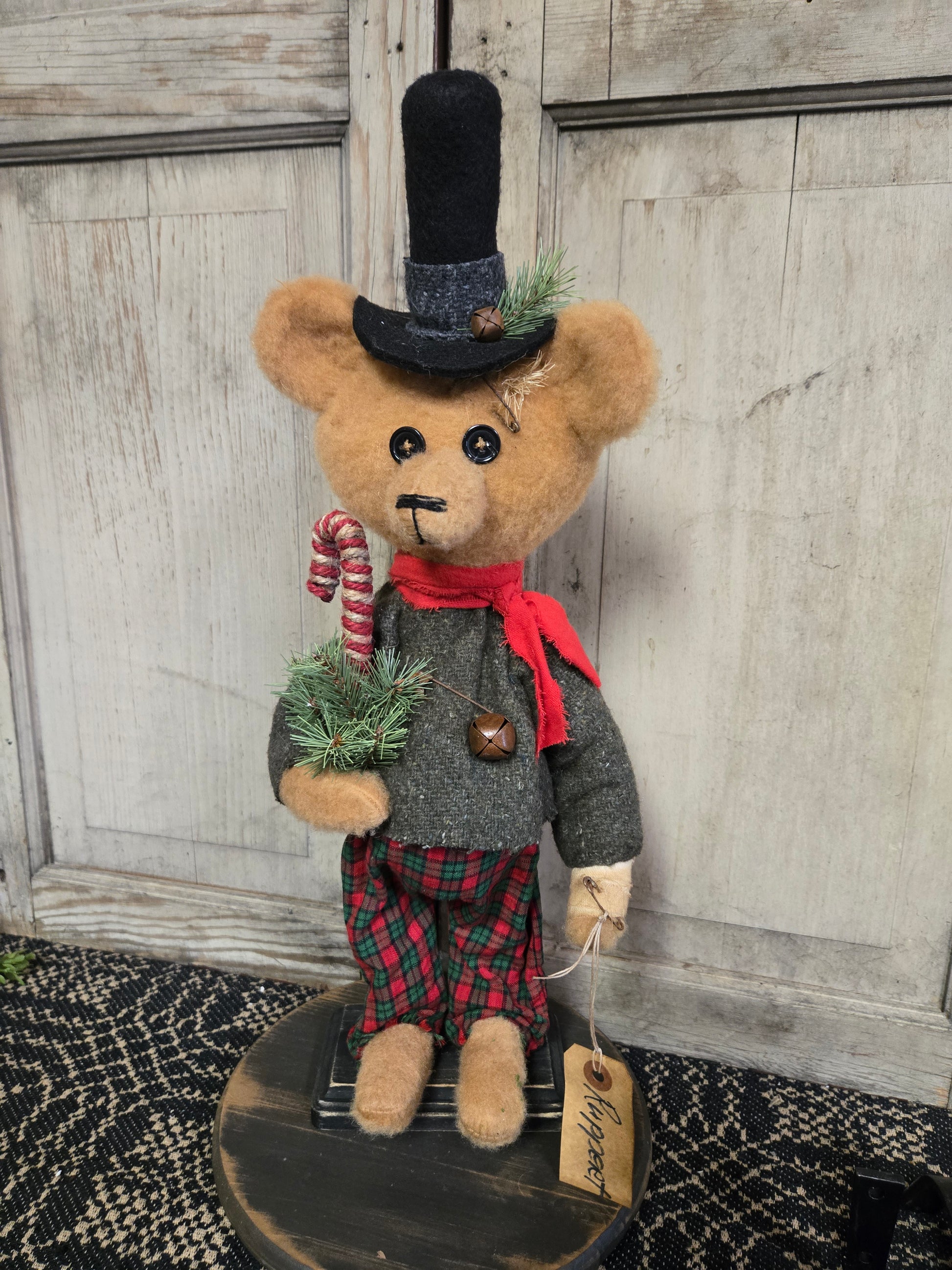A plush toy resembling a bear wearing a Santa hat and a scarf, standing on a round base.