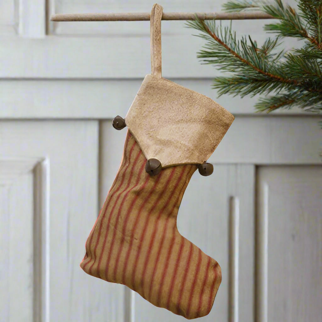 A red and white striped rustic Christmas stocking with a beige top and bell accents, displayed against a white background.