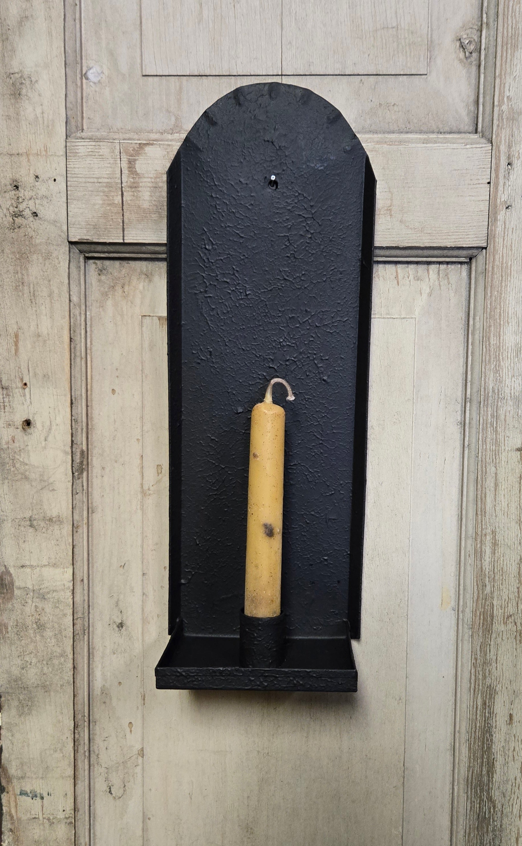 Black wall-mounted sconce with one candle on a wooden background