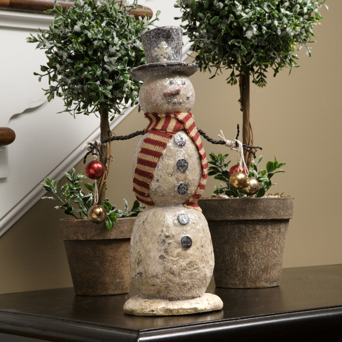 Decorative snowman figure with a striped scarf in front of potted plants.