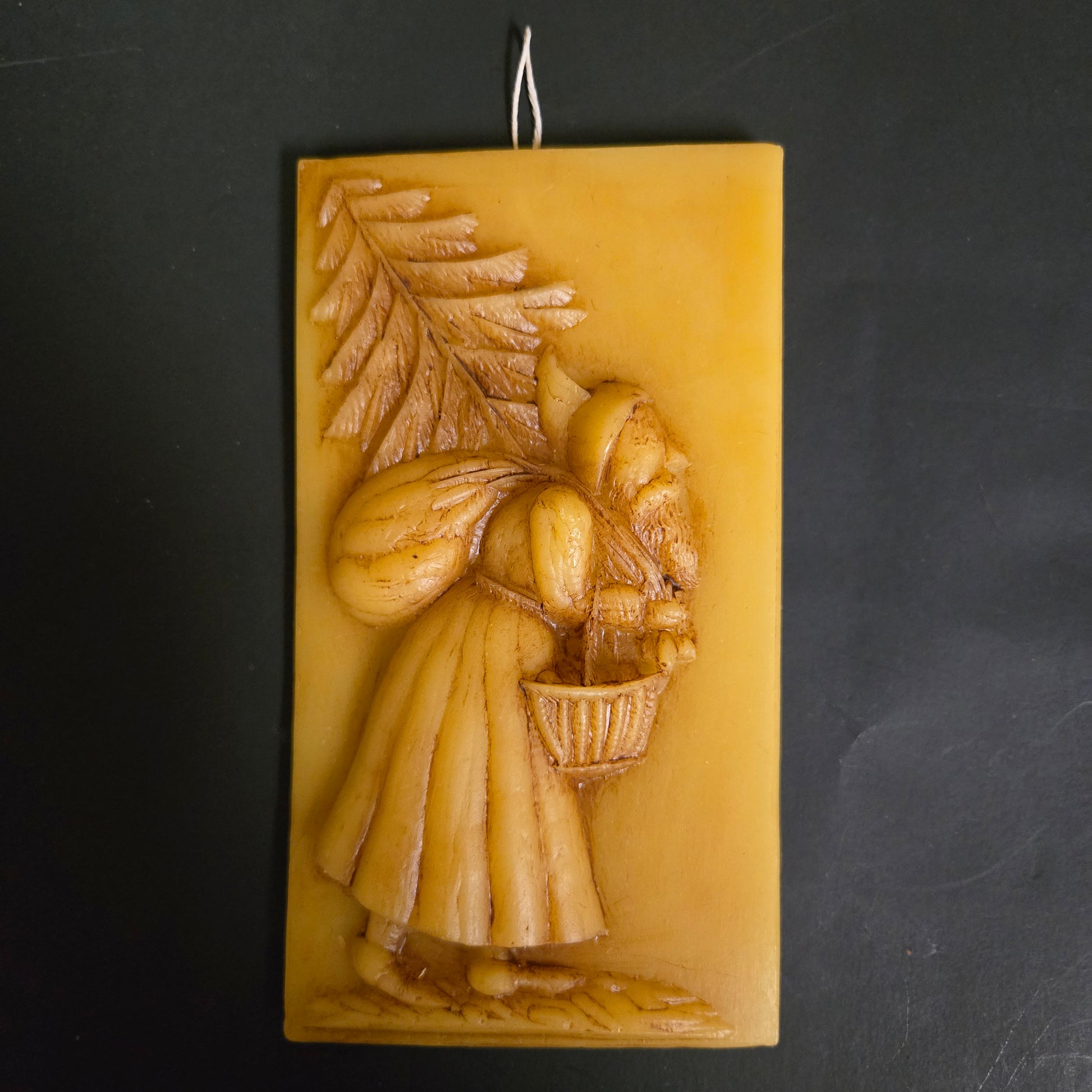 Pressed yellow beeswax of Santa with feather tree and basket on a dark background