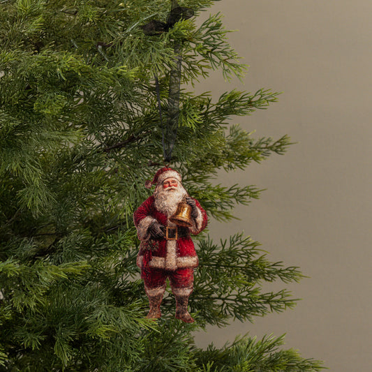 Santa Claus ornament hanging on a Christmas tree with a plain background
