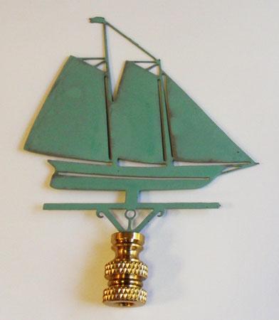 A copper lamp finial in the shape of a schooner sailboat with a verdigris finish, mounted on a gold-colored base.