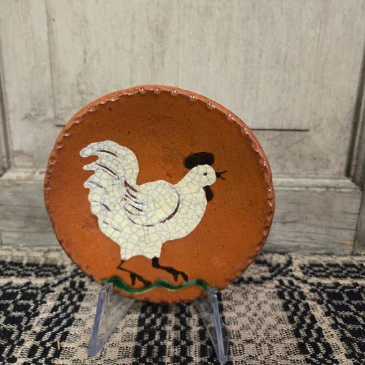 Small round redware plate featuring a white chicken with open beak standing on grass