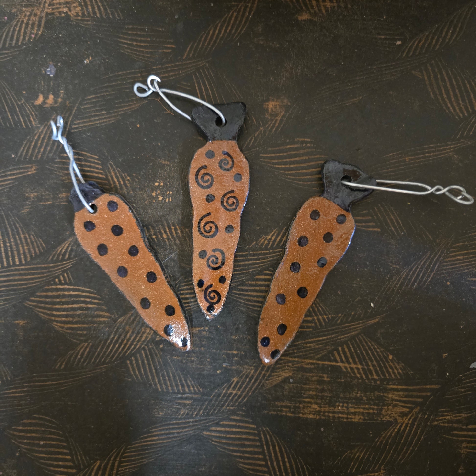 Three decorative stoneware pendants with patterns on a textured dark surface