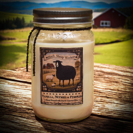 Mason jar candle with black sheep artwork on a wooden table in front of a farm scene