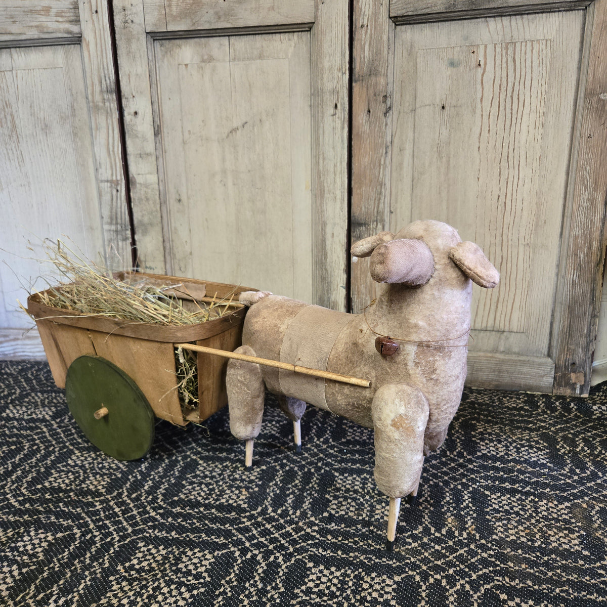 Sheep toy with a wheelbarrow filled with hay on a textured floor.