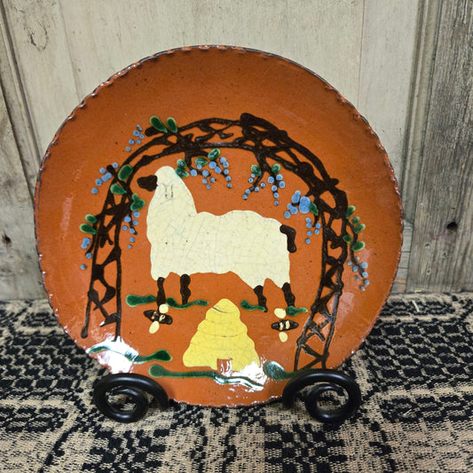 Redware plate with a sheep and bee skep underneath a flowering vine on trellis