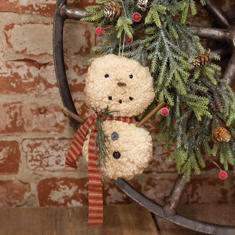 A Sherpa Snowbaby hanger with a red striped scarf and green sprig, displayed in a wheel-shaped frame with Christmas decorations around it.