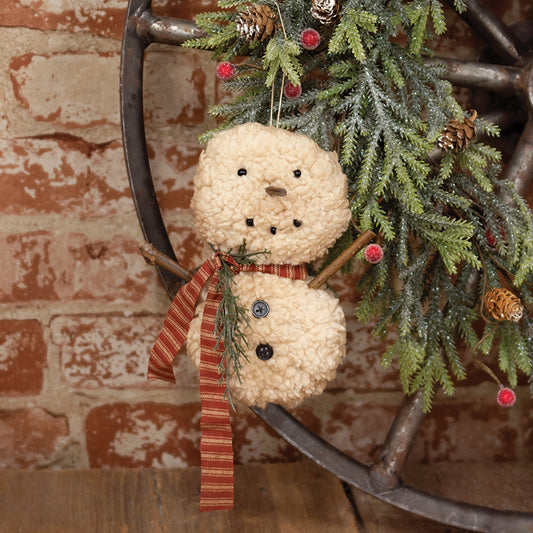 A Sherpa Snowbaby hanger with a red striped scarf and green sprig, displayed in a wheel-shaped frame with Christmas decorations around it.