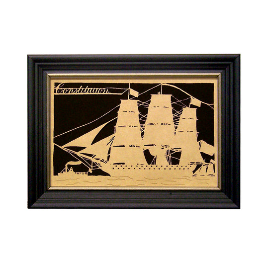 A framed artwork featuring a silhouette of a ship with a steamer and schooner, placed on a black paper stock within a black frame with gold edge.