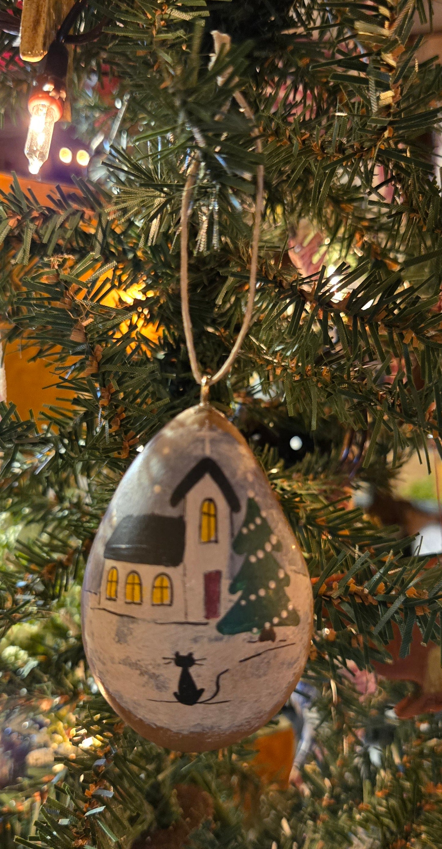 A handcrafted gourd ornament with a Christmas tree and house design, hanging from a tree.