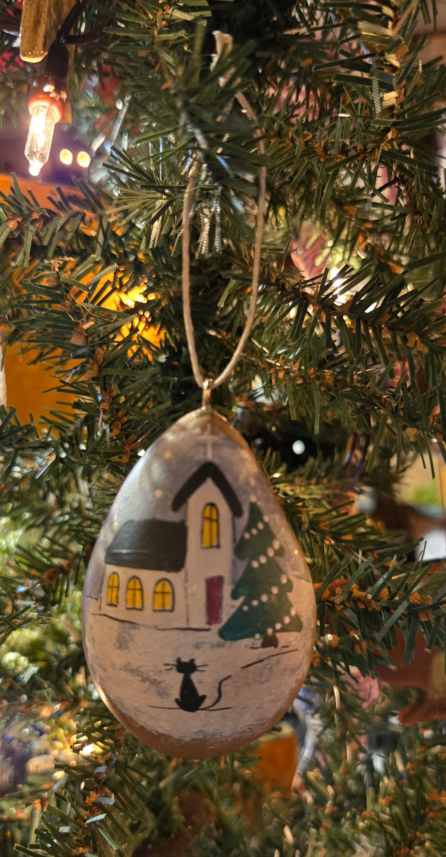 A handcrafted gourd ornament with a Christmas tree and house design, hanging from a tree.