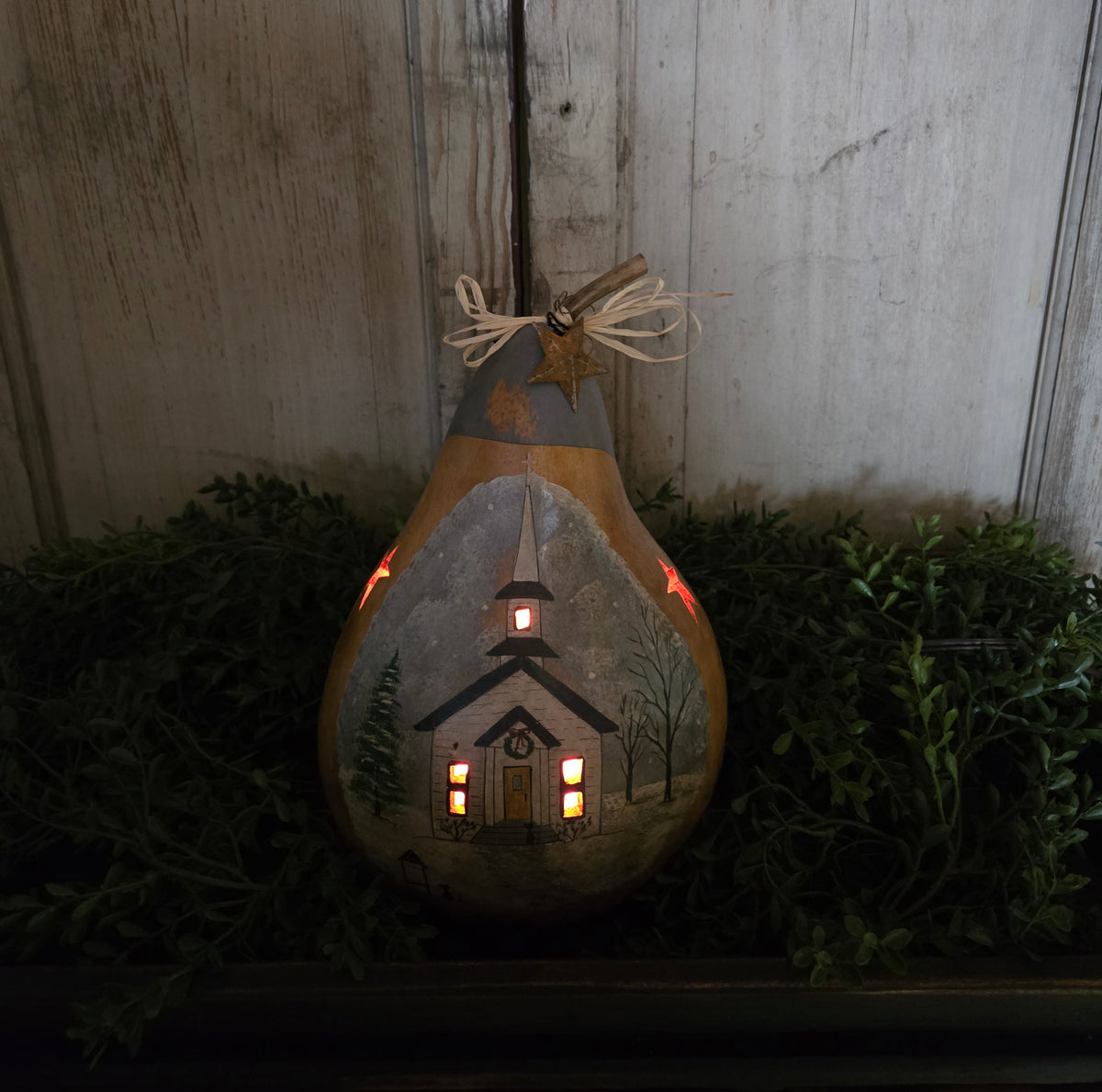 Lighted, carved gourd on a bed of greenery.