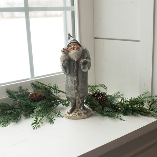 A silver figurine of Santa Claus with a snowman, placed on a windowsill with holiday decorations.