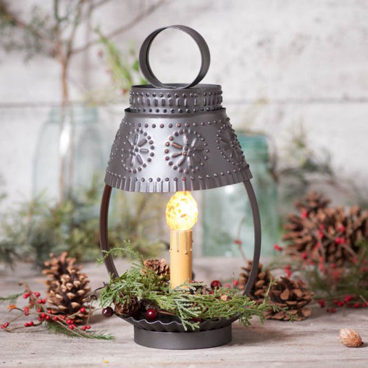 Decorative lantern with a lit bulb surrounded by pine cones and greenery on a wooden surface.