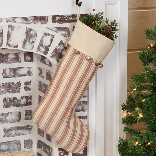 A Christmas stocking with vertical stripes in beige and dusty rose, hanging on a white doorframe next to a brick fireplace and a decorated Christmas tree.