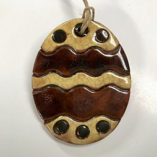 A handcrafted Egg Redware Ornament with a beige and brown color pattern, featuring circles and waves, used for holiday decor.