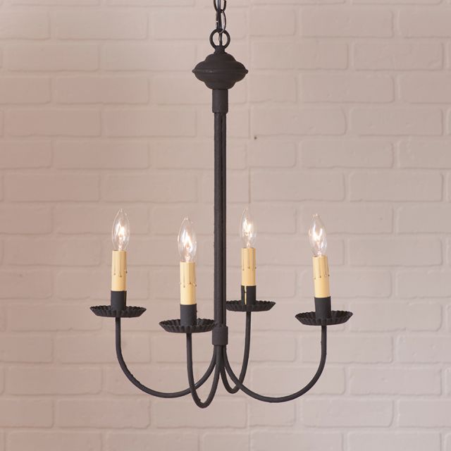 Black chandelier with four candle-style lights against a white brick wall.