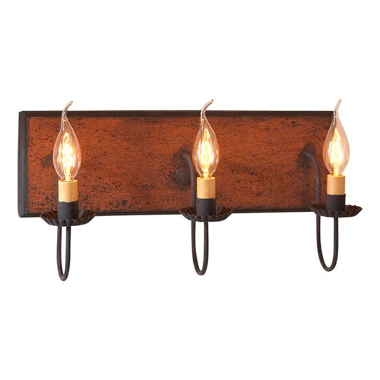 A vintage style vanity light with three bulbs, featuring a distressed pumpkin color over black with black stripe painted finish and textured arms with crimped pans.