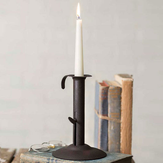 A black metal candle holder with a rustic design, placed on an open book, with a lit candle in it. The holder is adjustable and the candle is not included.