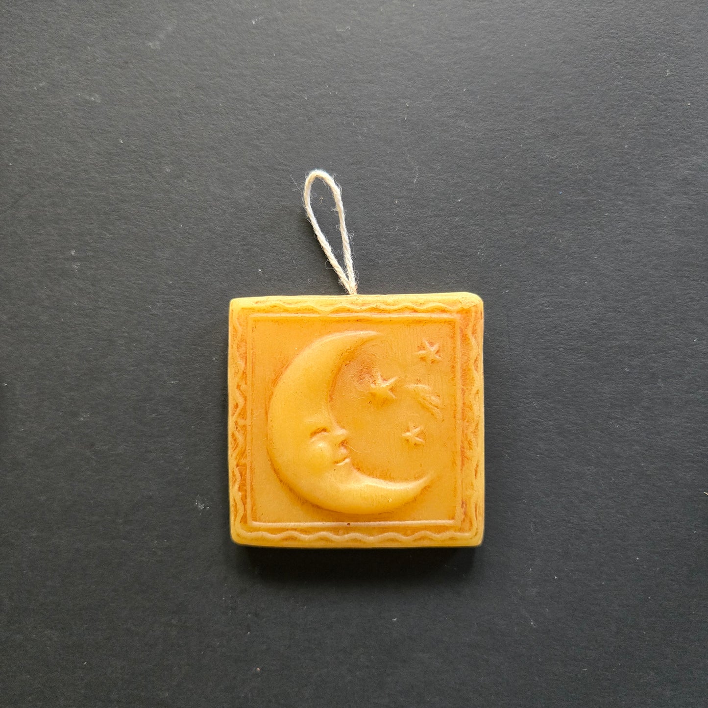 Decorative beeswax ornament with moon and star design on a dark background