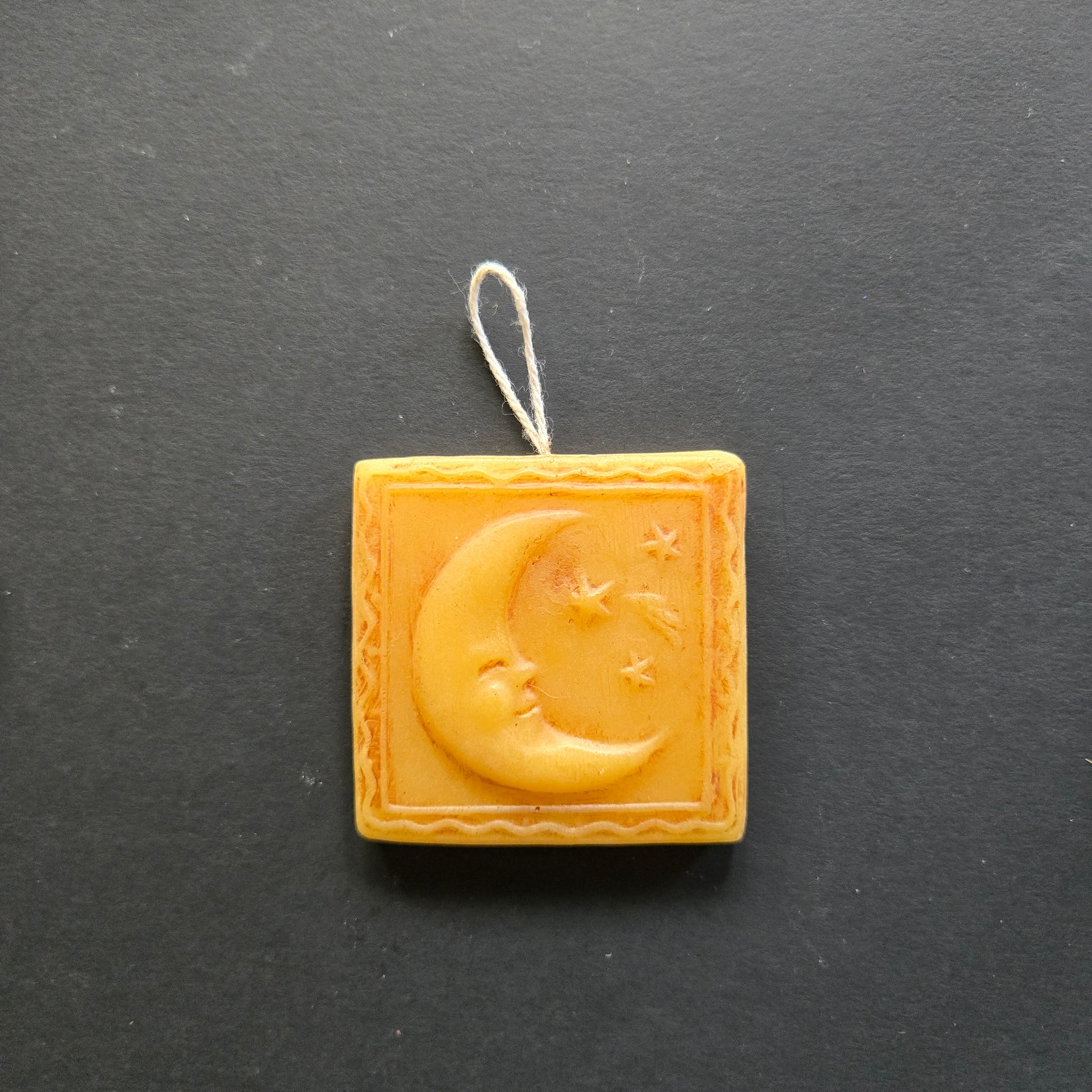 Decorative beeswax ornament with moon and star design on a dark background