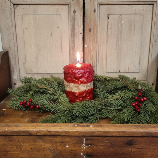 Red candle with greenery on a wooden surface against a wooden panel background