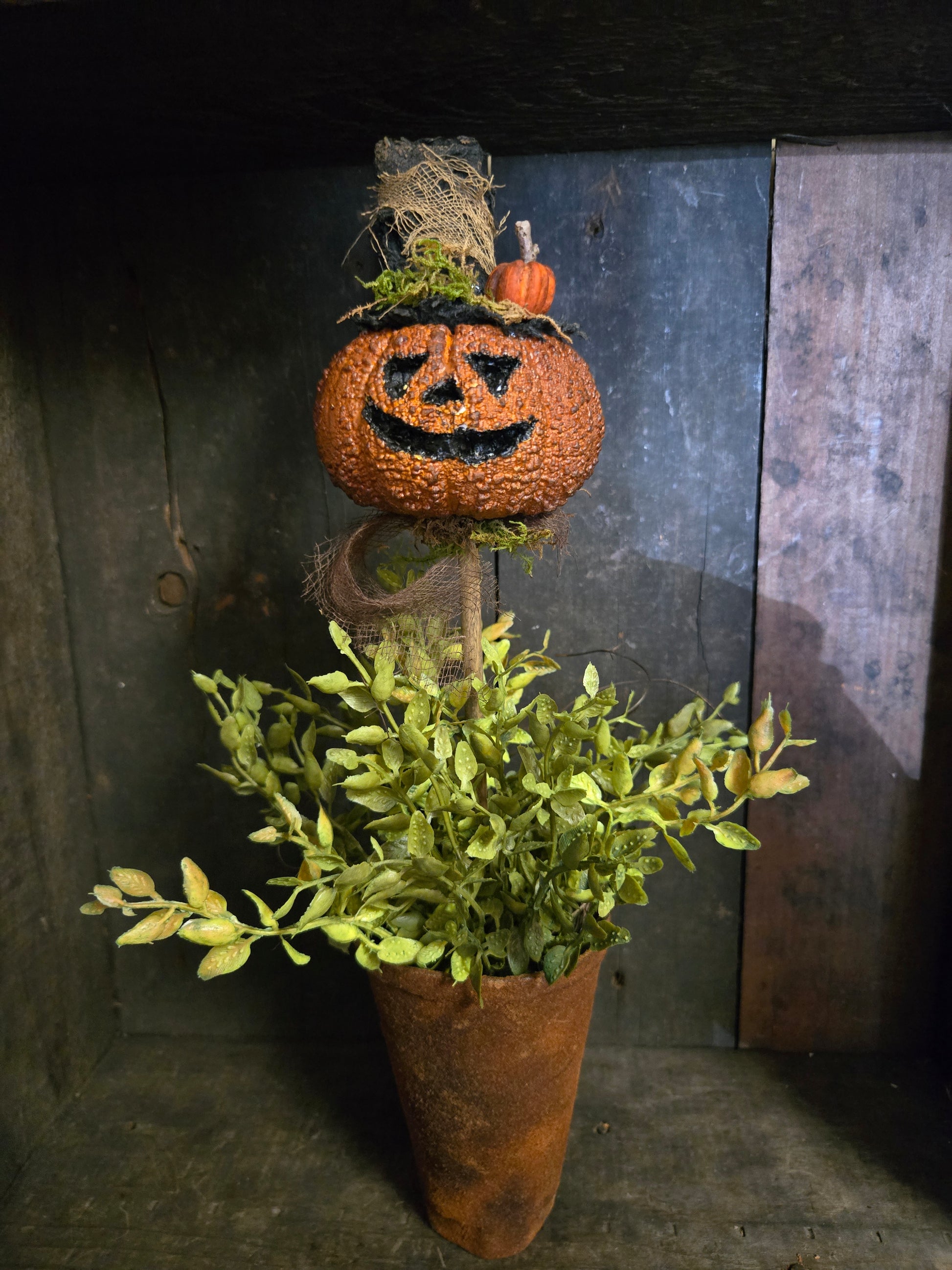 Decorative item with a carved pumpkin and greenery on a rustic wooden surface