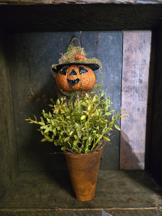 Potted plant with a Halloween-themed pumpkin topiary against a rustic wooden background