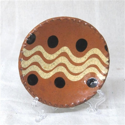 A small, round, red ceramic plate with a geometric pattern of lines and dots, displayed on a clear stand.