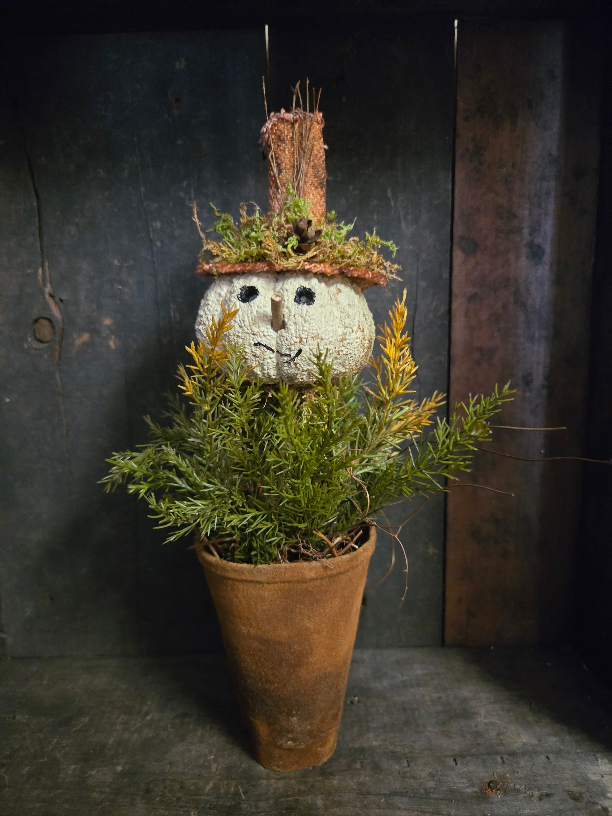 Decorative pumpkin head snowman with greenery on a dark surface