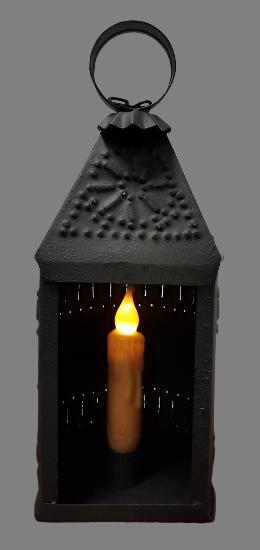 A black textured metal candle lantern with a candle lit inside, designed for use with a 4-inch taper candle (not included).