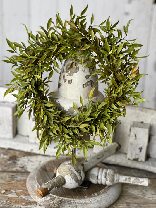 A green candle ring with tapering leaves arranged on a white surface, designed to hold a candle.