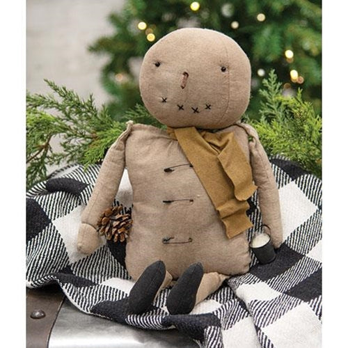 Snowman figure with a mustard scarf on a checkered blanket with a Christmas tree in the background