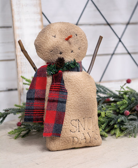 Stuffed snowman doll with a grungy fabric finish, orange carrot nose, plaid scarf, pine spray, and stick arms. It has 'Snow Days' text embroidered on its chest.